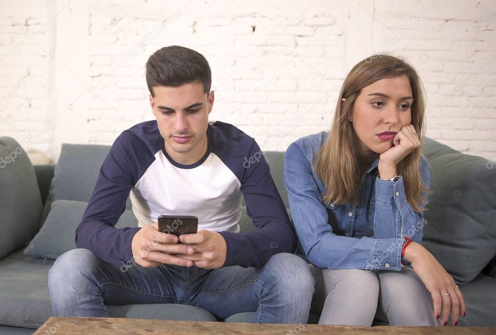 young attractive couple in relationship problem with internet mobile phone addiction boyfriend ignoring sad neglected and bored girlfriend 