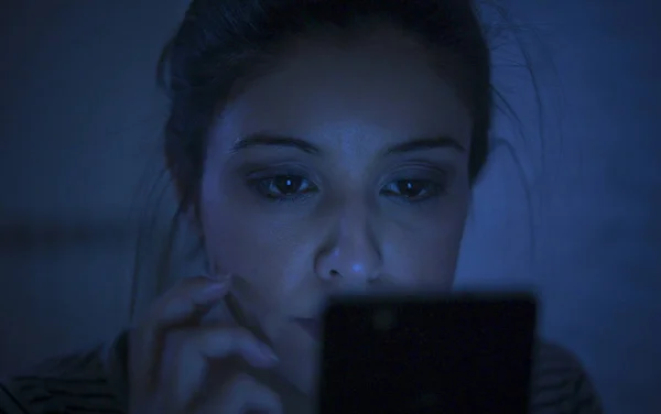 Potret wanita latin muda yang cantik menggunakan ponsel larut malam tanpa tidur berbaring di tempat tidur dalam gelap di smartphone dan internet kencan kecanduan aplikasi — Stok Foto
