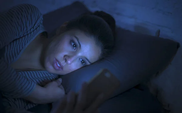 Potret wanita latin muda yang cantik menggunakan ponsel larut malam tanpa tidur berbaring di tempat tidur dalam gelap di smartphone dan internet kencan kecanduan aplikasi — Stok Foto