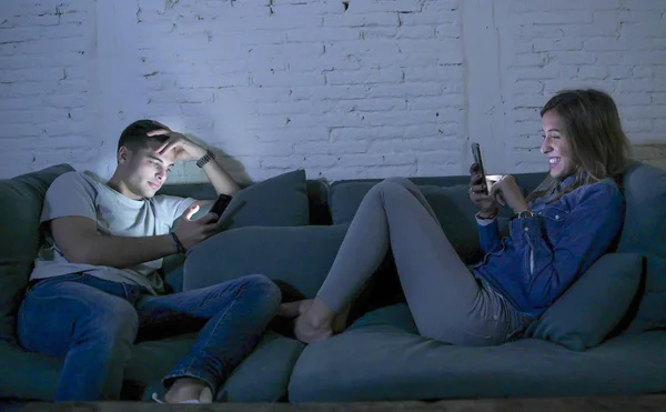 Молодая пара у себя дома диван улыбаясь счастливы вместе, но разделены игнорируя друг друга сосредоточены на мобильный телефон в интернет-зависимости — стоковое фото