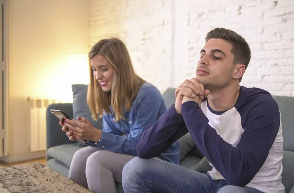 Jovem casal em casa sofá sofá com internet mulher e vício em celular ignorando seu namorado sentindo-se triste ciumento frustrado chateado — Fotografia de Stock