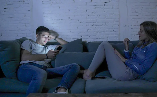 Pasangan muda di sofa rumah tersenyum bahagia bersama-sama tetapi terpisah mengabaikan satu sama lain berkonsentrasi pada ponsel telepon dalam kecanduan internet — Stok Foto