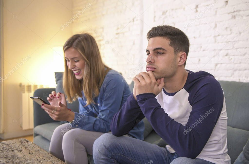 young couple at home sofa couch with woman internet and mobile phone addiction ignoring her boyfriend feeling sad jealous frustrated upset