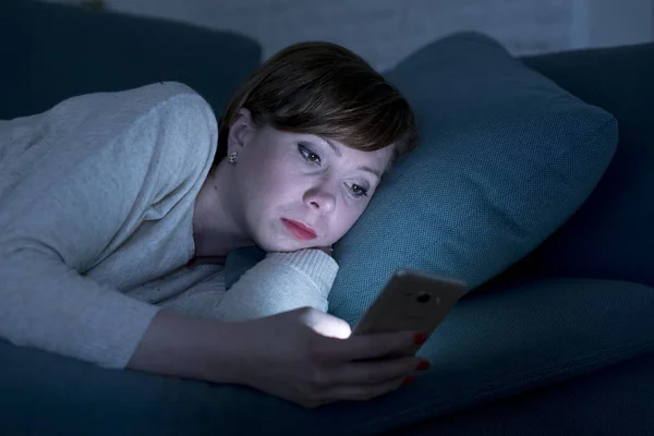 Retrato de mujer joven de 30 años acostada en el sofá de la cama tarde en la noche en casa utilizando la aplicación de redes sociales en el teléfono móvil cansado y soñoliento — Foto de Stock