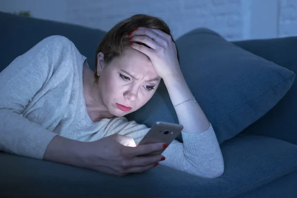 Retrato da jovem de 30 anos deitada no sofá cama tarde da noite em casa usando o aplicativo de mídia social no telefone celular cansado e sonolento — Fotografia de Stock