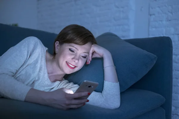 Jolie et heureuse femme rousse aux cheveux sur la vingtaine ou la trentaine couchée sur le canapé ou le lit à la maison en utilisant un téléphone mobile tard dans la nuit souriant dans la dépendance à Internet — Photo