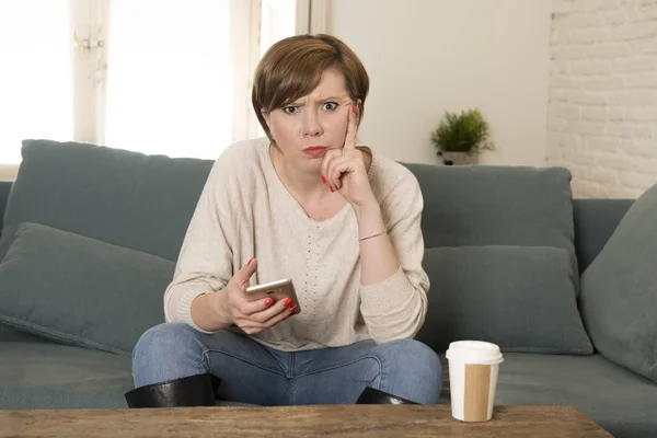 Молода приваблива 30s червоне волосся жінка засмучена нудною і примхливою, використовуючи інтернет-додаток на мобільному телефоні, сидячи на домашньому дивані в роздратованому вираженні обличчя — стокове фото