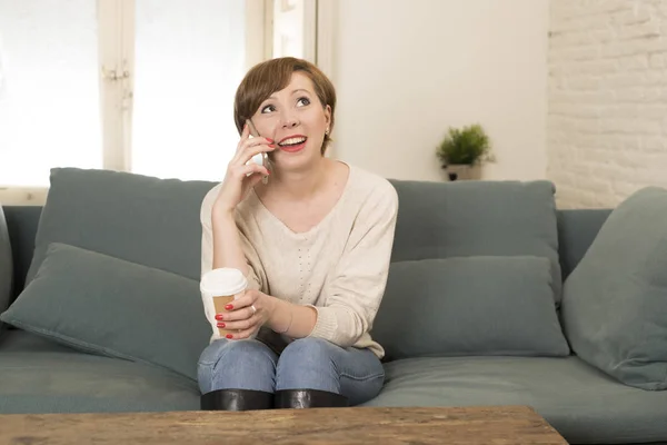 Młody atrakcyjny i szczęśliwy czerwone włosy kobieta siedzi w domu sofa kanapa picia kawy rozmowy na telefon komórkowy złagodzone w komunikacja koncepcja — Zdjęcie stockowe