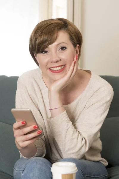 Muda menarik dan bahagia wanita rambut merah duduk di sofa rumah c — Stok Foto