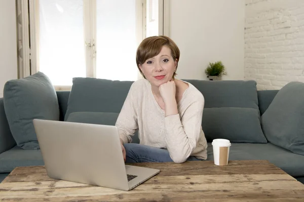 Wanita muda yang menarik dan bahagia di sofa rumah melakukan beberapa pekerjaan komputer laptop tersenyum santai dalam gaya hidup pengusaha — Stok Foto