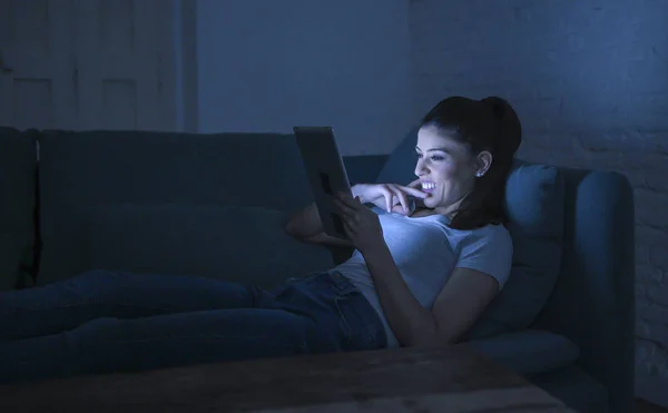Fiatal szép boldog és nyugodt latin nő 30-as években feküdt otthon kanapén késő esti segítségével digitális eszköz laptop tabletta pad internet film mosolyog néz — Stock Fotó