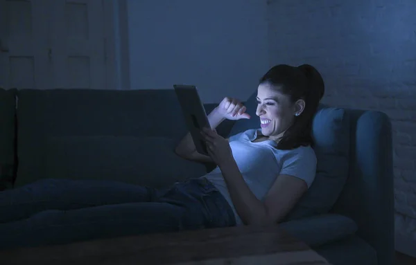 Muda cantik bahagia dan santai perempuan latin 30-an berbaring di sofa rumah larut malam menggunakan perangkat digital laptop pad menonton film internet tersenyum — Stok Foto