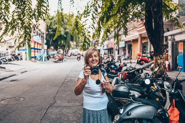 Elderly senior Asian traveling backpacker mature woman tourist walking enjoying taking photos in Sanya local street outdoor. Traveling along Asia, active lifestyle concept. Discovering Hainan, China