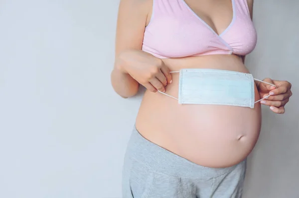 Tanımlanamayan hamile kadının yüz maskesi tutan ve karnındaki koca bebeği gösteren portresi. Hamilelik, annelik, doğmama ve beklenti konsepti. Metin modeli için boş alan