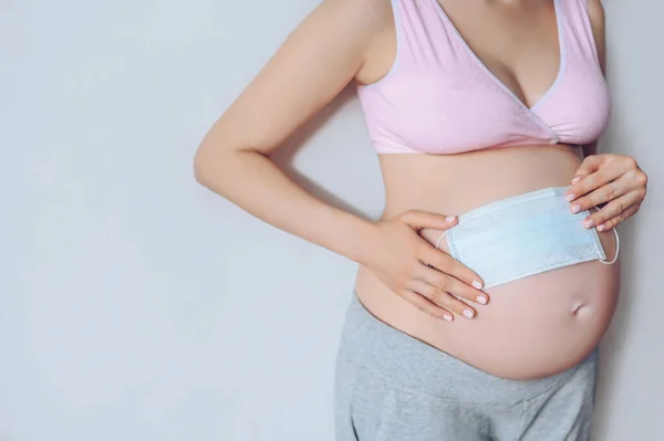 Tanımlanamayan hamile kadının yüz maskesi tutan ve karnındaki koca bebeği gösteren portresi. Hamilelik, annelik, doğmama ve beklenti konsepti. Metin modeli için boş alan