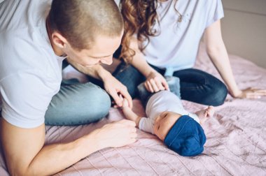 Bebeğini kucağında tutan mutlu ebeveynlerin yakın portresi. Genç, mutlu bir aile, anne ve baba yatak odasında yeni doğmuş tatlı bir çocukla oynuyorlar.