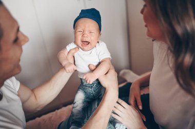 Ağlayan bebeklerini kucağında tutan mutlu ebeveynlerin yakın portresi. Genç, mutlu bir aile, anne ve baba yatak odasında yeni doğmuş tatlı bir çocukla oynuyorlar.