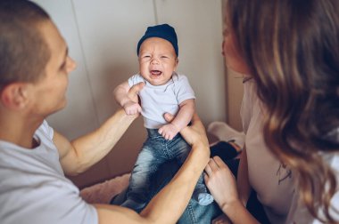 Ağlayan bebeklerini kucağında tutan mutlu ebeveynlerin yakın portresi. Genç, mutlu bir aile, anne ve baba yatak odasında yeni doğmuş tatlı bir çocukla oynuyorlar.