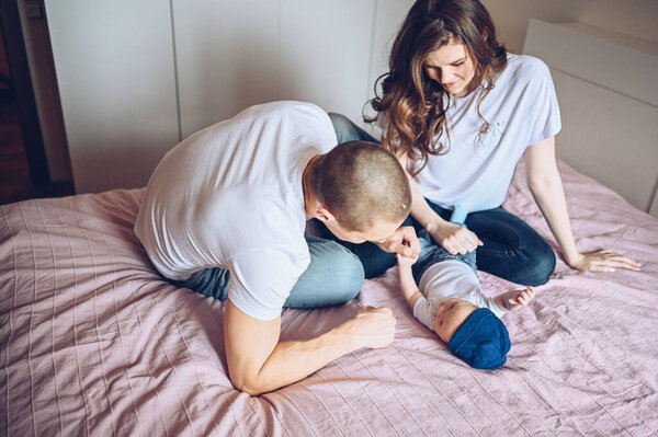 Close up portrait of a happy parents holding their baby. Young happy family, mom and dad playing with cute emotional little newborn child son in the bedroom