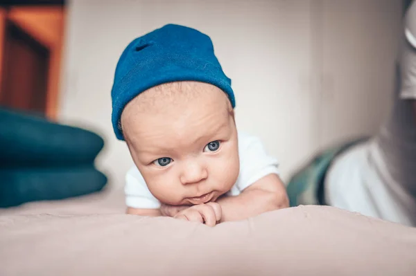 可爱的小男孩躺在卧室粉红色的毛毯上 新生儿 婴儿在床上保持清醒 穿着蓝色牛仔裤 蓝色帽子和白色T恤的有感情的新生儿的肖像 — 图库照片