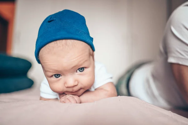 ベッドルームでピンクの毛布の上に寝そべってる可愛い赤ちゃん 新生児 赤ん坊はベッドの上で起きている 青いジーンズ 青い帽子 白いTシャツの中の感情的な新生児の肖像 — ストック写真