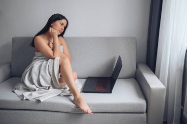 Güzel bir kadın dizüstü bilgisayar kullanıyor, video görüşmesi yapıyor, internette çalışıyor, e-posta yazıyor, sosyal ağ veya film izliyor, evdeki sıcak battaniyenin altında rahat bir gri koltukta oturuyor. Kişisel tecrit