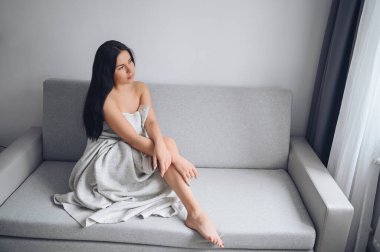 Evdeki sıcak battaniyenin altında rahat gri koltukta oturan güzel, sıska esmer kadın. Corona virüsü salgını sırasında kendini karantinaya al. COVID19 evde kalıp hayat kurtarma kavramı