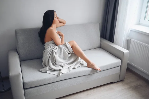 美しい退屈スレンダーなブルネットの女性は自宅で暖かい毛布の下に快適なグレーのソファに座っている コロナウイルスパンデミックの間の自己隔離隔離 Covid19 ホームセーブライフコンセプト — ストック写真