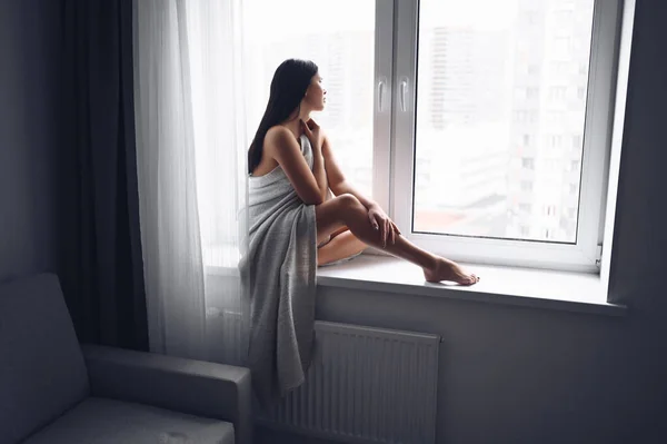 美しい退屈スレンダーなブルネットの女性は家で暖かい灰色の毛布の下で窓の横に座っている コロナウイルスパンデミックの間の自己隔離隔離 Covid19 ホームセーブライフコンセプト — ストック写真