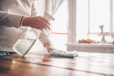 Ev ahşap masayı temizlemeyi, mutfak masasının yüzeyini dezenfektan antibakteriyel sprey şişesiyle temizlemeyi, yüzeyi havlu ve eldivenle yıkamayı. COVID-19 önleme içeride dezenfekte ediliyor.