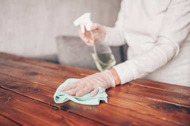 Ev ahşap masayı temizlemeyi, mutfak masasının yüzeyini dezenfektan antibakteriyel sprey şişesiyle temizlemeyi, yüzeyi havlu ve eldivenle yıkamayı. COVID-19 önleme içeride dezenfekte ediliyor.