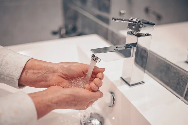 Hand washing lather liquid soap rubbing wrists handwash step senior woman rinsing in water at bathroom faucet sink. Wash hands for COVID-19 spreading prevention. Coronavirus pandemic outbreak.