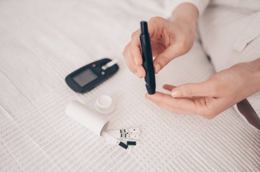 Diyabet, kan şekerini ölçüyor. Evde Lancelet ve dijital glukometre kullanan bir kadın. İlaç, diyet diyabet, sağlık bakımı konsepti - glukometreyle kadın elleri vücut glikozu seviyesini kontrol ediyor