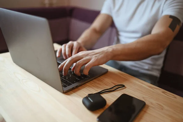 Young european man hands with smartphone and headphones working on a laptop during coronavirus isolation home quarantine. Covid-19 pandemic Corona virus. Distance online work from home concept.