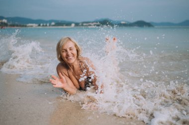 Mutlu gülümseme, yaşlı turistleri heyecanlandırdı. Suda oynayıp okyanus sahilindeki büyük dalgalarda yüzüyorlar. Asya boyunca seyahat, aktif yaşam tarzı konsepti.