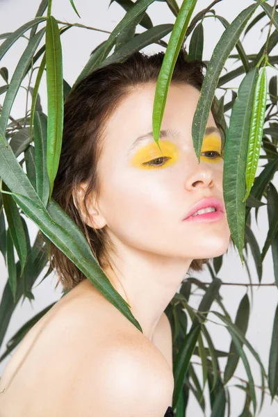 Excited young girl smiling with perfect skin and teeth with fresh yellow color makeup and green plant. Natural beauty woman amazed. Expressive facial expressions. Skincare beauty spa treatment concept