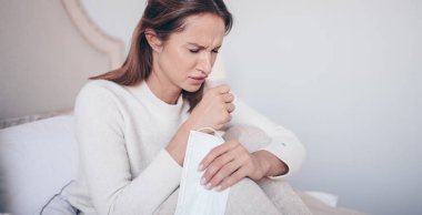 Coronavirus hastalığı (COVID-19) belirtileri - burun akıntısı, boğaz ağrısı, öksürük, ateş. Yüzü maskeli genç bir kadın grip virüsünden hasta. Evde karantina altında yatan Corona virüsü yayıyor.