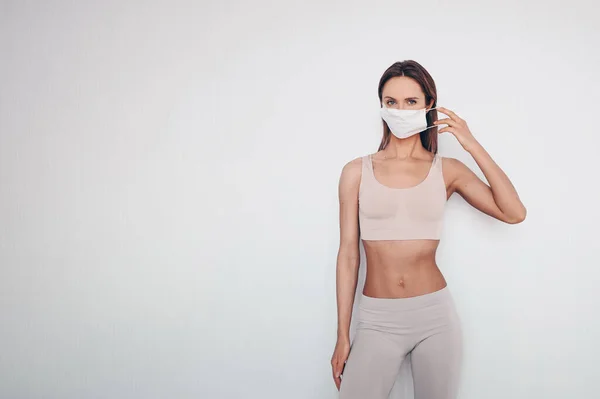 Home fitness. Young fit slim woman in sportswear protection face mask posing during self isolation quarantine. COVID-19 concept to promote stay safe home save lives. Free space for text mockup banner