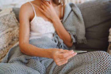 Tanınmayan hasta bir kadın elinde termometre ve haplarla kanepeye oturmuş kendini karantinaya almış. Evden uzaklık çevrimiçi işi. Corona virüsü enfeksiyonu COVID-19 konsepti. Evden uzak çalışma