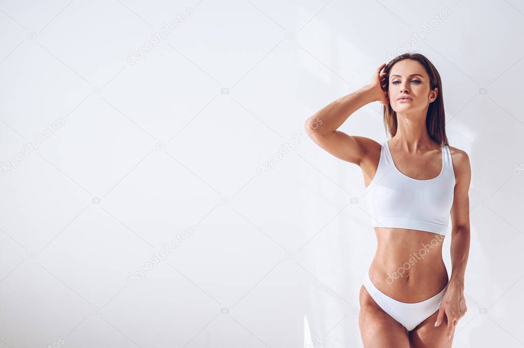 Young fit woman in white lingerie on white background isolated. Muscular slim attractive female with flat belly. Copy space for text. Body care, healthy and sporty life, hair removal, yoga concept