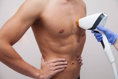 Pürüzsüz ciltli kaslı bir sporcu. Güzellik salonunda saç dökülmesi ve epilasyon. Erkek lazer tüyü çıkarma konsepti. İşlemler için modern aletleri kullanan bir güzellik uzmanı. Deri ve Güzellik Bakımı