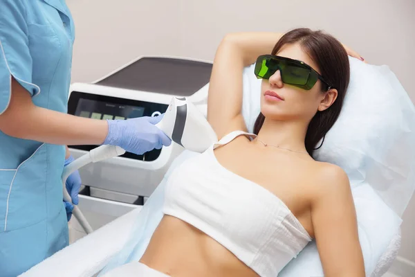 Güzellik salonunda lazer epilasyonu ve kozmetoloji. Saç çıkarma prosedürü. Lazer epilasyonu, kozmetoloji, spa ve saç temizleme konsepti. Güzel esmer kadın koltukaltında saç kesiliyor.