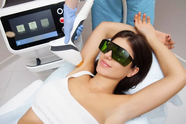 Güzellik salonunda lazer epilasyonu ve kozmetoloji. Saç çıkarma prosedürü. Lazer epilasyonu, kozmetoloji, spa ve saç temizleme konsepti. Güzel esmer kadın koltukaltında saç kesiliyor.