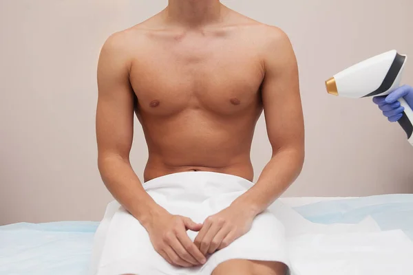Pürüzsüz ciltli kaslı bir sporcu. Güzellik salonunda saç dökülmesi ve epilasyon. Erkek lazer tüyü çıkarma konsepti. İşlemler için modern aletleri kullanan bir güzellik uzmanı. Deri ve Güzellik Bakımı