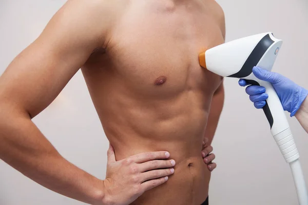 Pürüzsüz ciltli kaslı bir sporcu. Güzellik salonunda saç dökülmesi ve epilasyon. Erkek lazer tüyü çıkarma konsepti. İşlemler için modern aletleri kullanan bir güzellik uzmanı. Deri ve Güzellik Bakımı