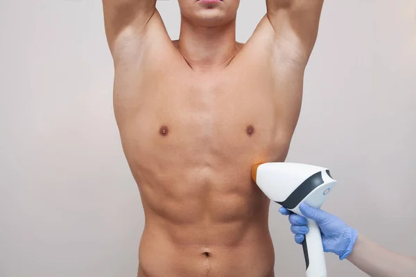 Pürüzsüz ciltli kaslı bir sporcu. Güzellik salonunda saç dökülmesi ve epilasyon. Erkek lazer tüyü çıkarma konsepti. İşlemler için modern aletleri kullanan bir güzellik uzmanı. Deri ve Güzellik Bakımı