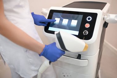 Lazer tüy çıkarma aleti ve tıbbi eldivenler giymiş bir güzellik uzmanının elleri. Epilasyon ve spa konsepti