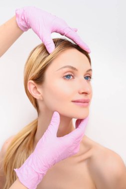 Eldivenli güzellik uzmanları genç bir kadının yüzüne dokunuyor. Estetik ameliyat konsepti. Yüz güzelliği. Mükemmel makyajlı ve yumuşak tenli güzel sarışın kadın portresi..