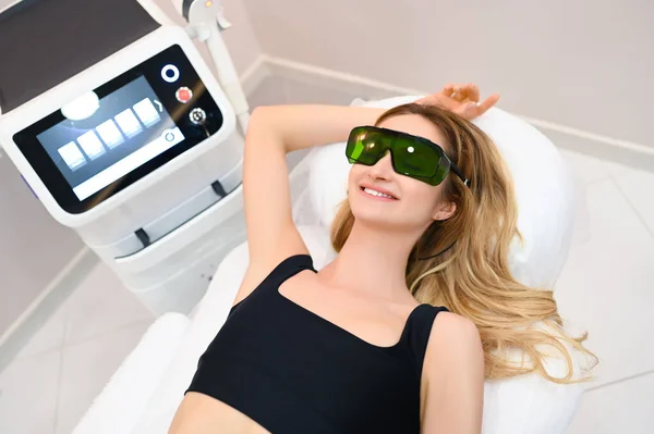 Güzellik salonunda lazer epilasyonu ve kozmetoloji. Saç çıkarma prosedürü. Lazer epilasyonu, kozmetoloji, spa ve saç temizleme konsepti. Güzel sarışın kadın koltuk altlarını aldırıyor.