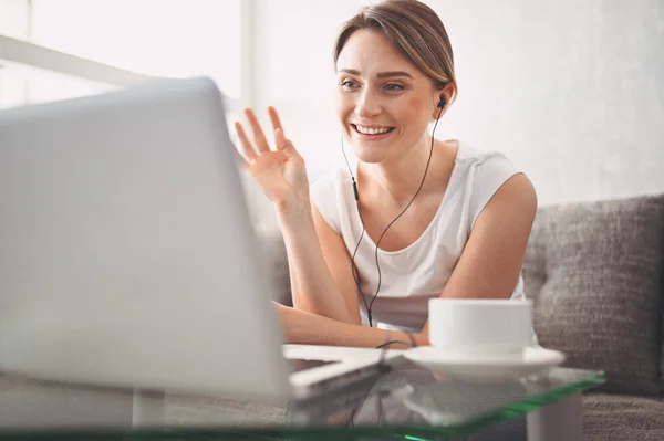 Çekici mutlu genç öğrenci evde online çalışıyor, dizüstü bilgisayar, kulaklık kullanıyor, görüntülü konuşma yapıyor, el sallıyor. Uzaktan çalışma, uzaktan eğitim. Karantina ile ilgili video konferansı veya sanal olay